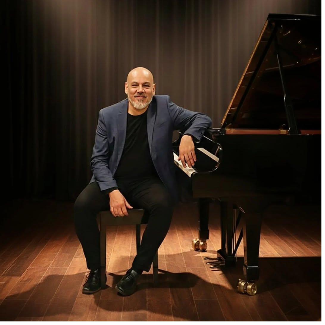 Juan Rivero, composer, beside a grand piano